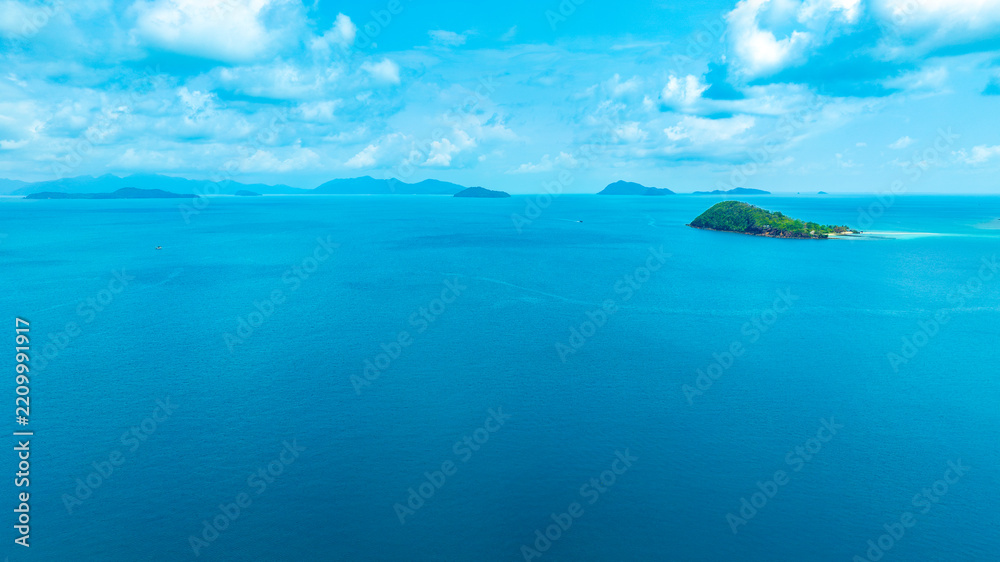 Naklejka premium Panoramic aerial view of a lush green tropical island in the middle of a vast blue ocean under a bright sky with clouds, representing vacation, travel, and scenic nature.concept travel 