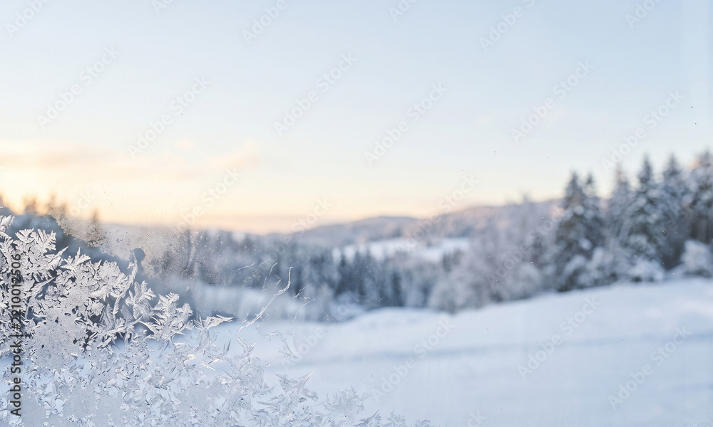 Obraz premium Frosty window pane looking out over a snowy winter landscape at sunrise