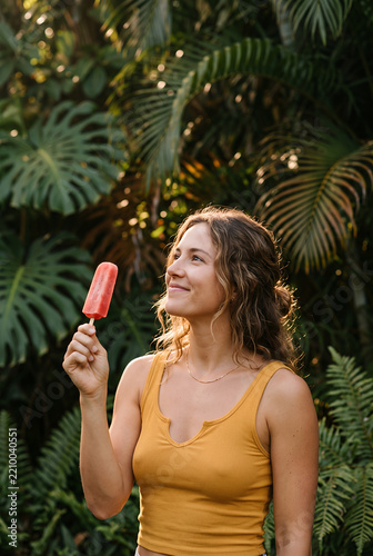 Young Asian woman holding popsicle in tropical garden setting