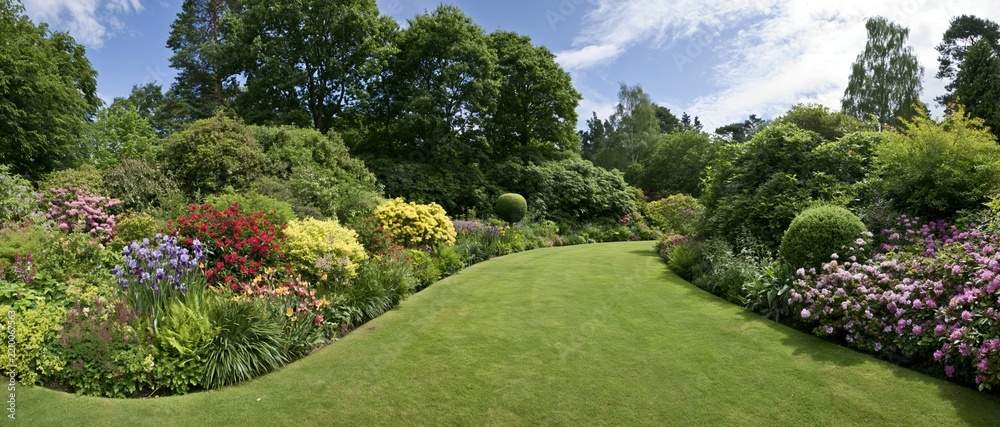 Obraz premium A curving green lawn bordered by colorful blooming flowers and shrubs in a well-maintained garden