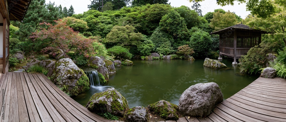 Obraz premium Traditional japanese garden with still koi pond surrounded by moss-covered rocks and wooden pathways