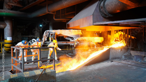 Fotografie Steel plant workers operating a high-temperature blast furnace with glowing molten metal tapping stream
