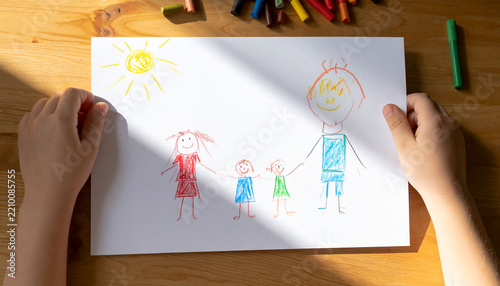 Child drawing a colorful family picture by hand with crayons on a wooden table
木の机でクレヨンを使って家族の絵を描く子どもの手元