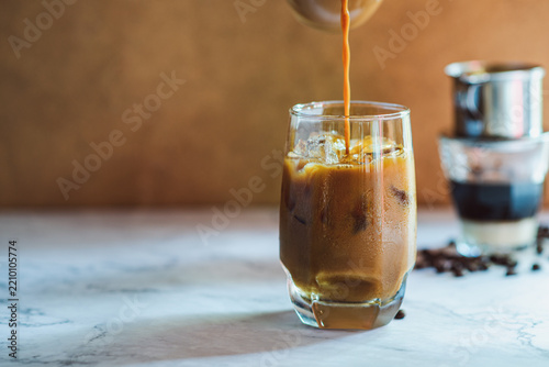 Pouring coffee into a glass of Vietnamese iced coffee with condensed milk and ice cubes.