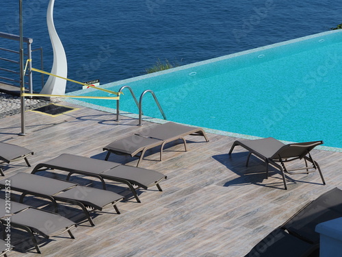 View of the infinity pool with sun loungers against the backdrop of the sea, and the hotel grounds.