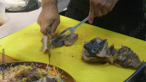 Chef slicing cooked meat for Uzbek plov beside plate of finished pilaf