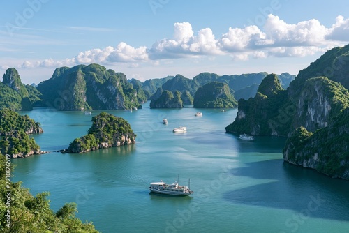 Elevated view of Halong Bay with limestone karsts covered in lush green vegetation rising from turquoise waters, several tourist boats cruising between the islands under bright sunny skies with
