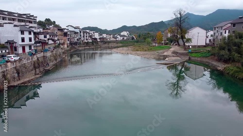 Traditional Chinese Water Town with White Houses Along a Calm River Under a Cloudy Sky in China