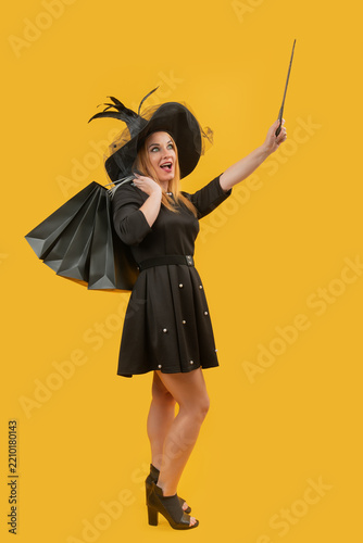Fotografie Woman dressed in a witch hat and black dress holding shopping bags and a magic w