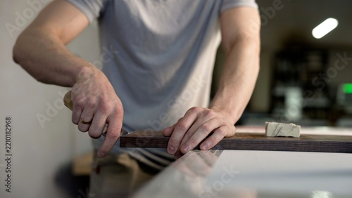 Carpenter's hands carefully finishing edge of dark wood board with hand tool in workshop, skilled manual labor