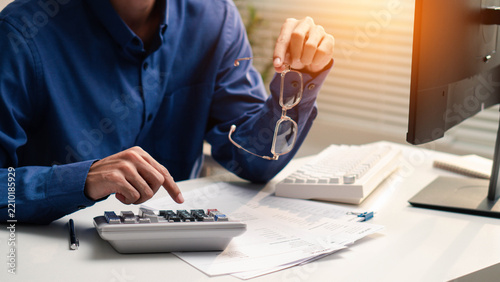 Close-up of a person using a calculator while holding eyeglasses over financial documents, illustrating debt review, expense tracking, budget planning, accounting, payment, and financial management.