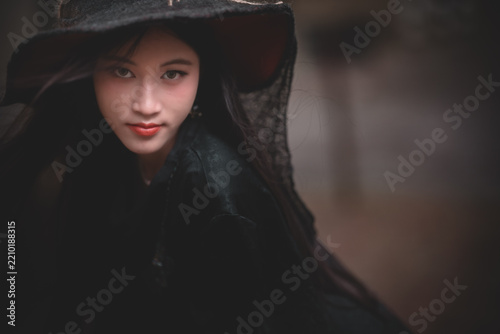 Fotografie Moody Woman in Black Hooded Gothic Cloak Witch costume Halloween Themes
