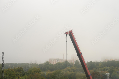 A construction crane stands tall against a foggy backdrop. The scene includes trees and buildings partially obscured by mist, creating a sense of depth and space.
