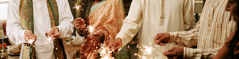Obraz premium Header of Indian family holding sparkling sparklers during festival celebration together indoors. Scene suitable for holiday marketing campaigns and cultural event promotions