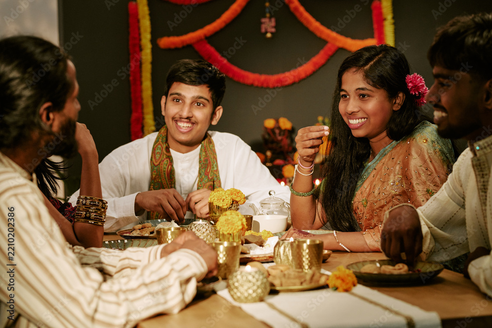 Obraz premium Asian Indian young adults and teenager smiling, celebrating traditional festive holiday together at dining table. Concept suitable for cultural marketing and holiday advertising campaigns