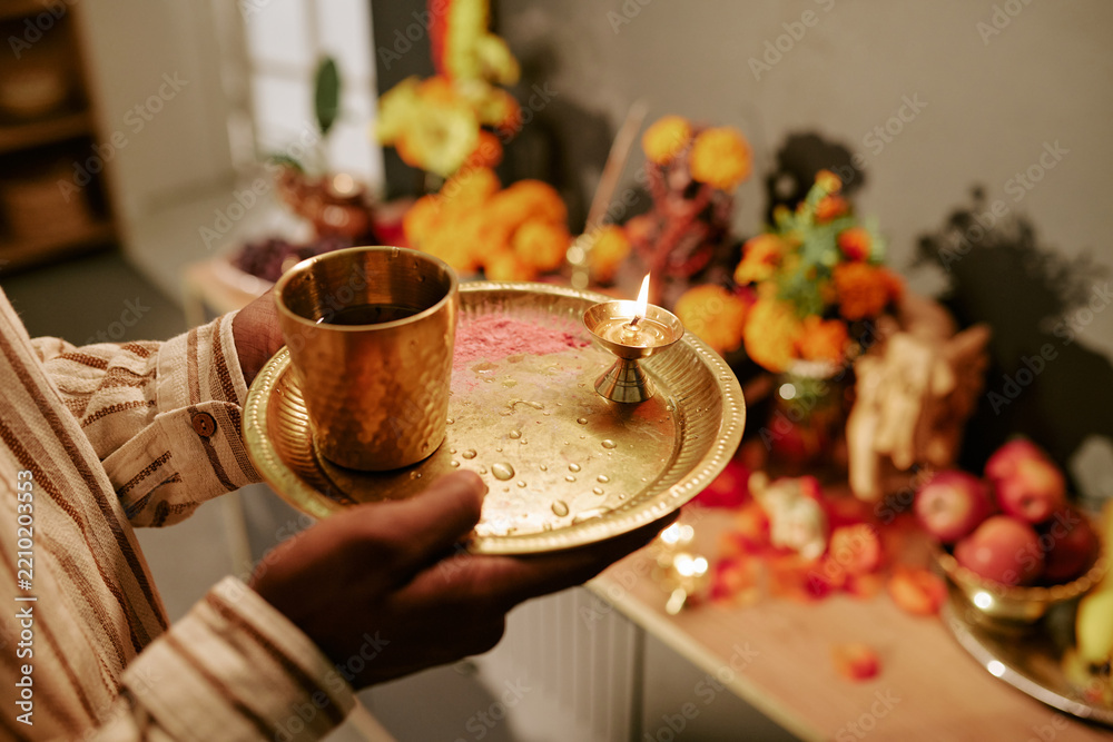 Obraz premium Cropped hands of Indian young adult man holding traditional brass pooja thali with burning oil lamp during Diwali celebration. Useful for festive religious marketing and cultural projects