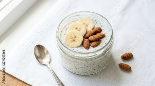 Healthy chia seed pudding in a glass jar topped with fresh banana slices and whole almonds, isolated on white background