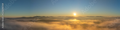Panorama aerial view of a sea of fog over morning countryside under clear sky with sun