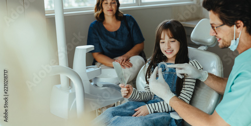 Girl views dental alingers with dentist and mother in clinic