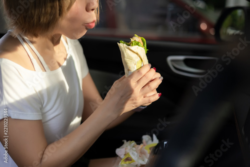 Woman is eating breakfast while sitting in a car in the morning