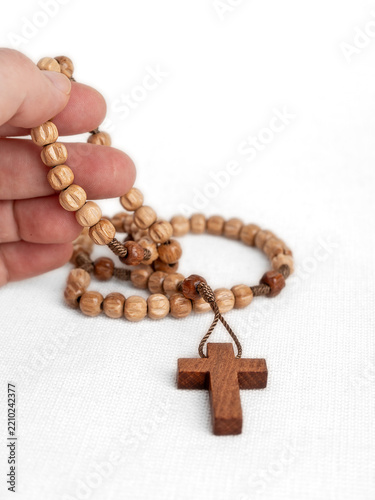 Obraz na plátně Hand Holding Wooden Rosary and Cross on White Background