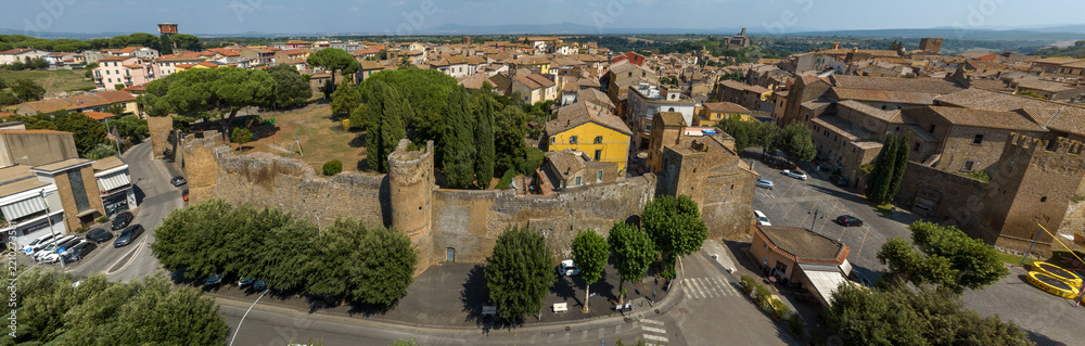 Obraz premium Panoramic aerial view of the medieval walls and round towers of Tuscania, in the province of Viterbo, in Lazio, Italy, with umbrella pines, cypresses, roads and the rooftops of the historic center.