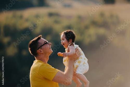 Father Lifting Laughing Baby Outdoors at Sunset — Playful Family Moment and Parental Joy