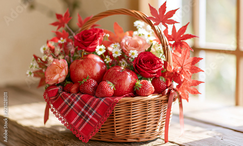 A wicker basket filled with shiny red apples, juicy ripe strawberries, red and pink roses