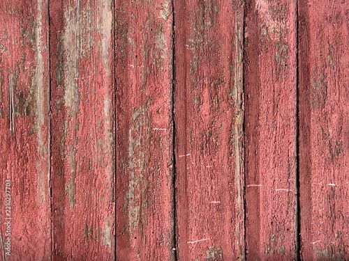 Weathered red wooden siding with peeling cracked paint, chipped edges, nail holes, and layered patina on vertical planks, rustic exterior wall