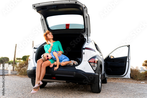 Mother and daughter relaxing in car trunk during summer road trip vacation
