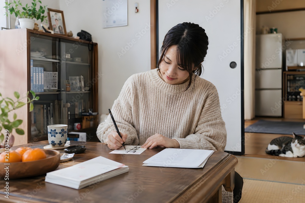 Obraz premium 座卓で年賀状を書く女性