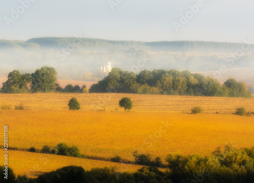 Church and golden fields at the autumn foggy morning