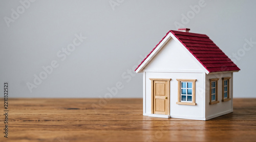 Miniature white house with red roof on a wooden surface, symbolizing home, real estate, and property ownership concepts