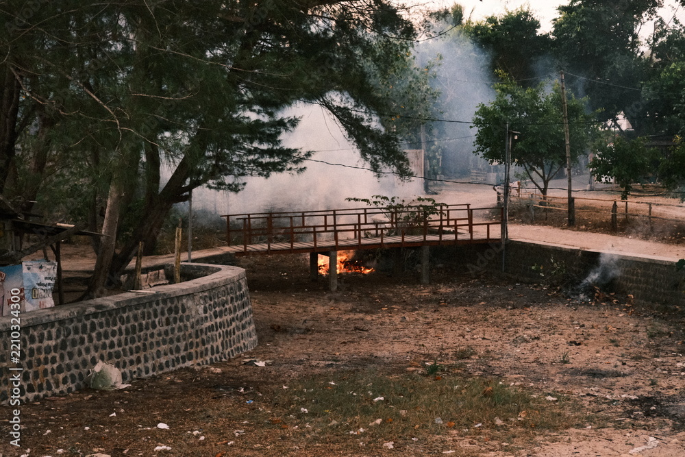 Fototapeta premium Open burning of waste under a small wooden bridge