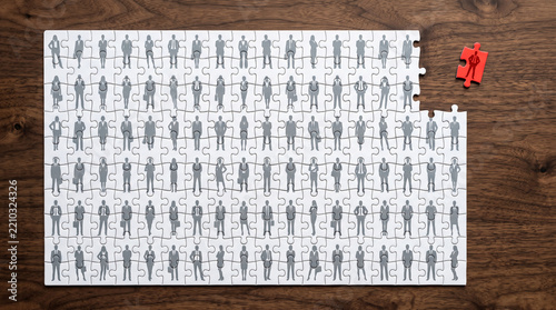 Puzzle pieces with grey silhouette of people arranged, one red piece separate, symbolizing team unity, recruitment, and business solutions