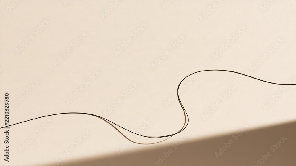 Fototapeta premium A pale beige minimal Halloween background uses one thin black cord arranged into a loose abstract curve reminiscent of a spiderweb strand, with crisp studio shadows and no additional props
