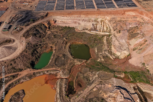 Aerial view of an open-pit mine featuring discolored industrial waste ponds in shades of green, brown, and orange, surrounded by barren mining terrain in Welkom, Free State, South Africa.