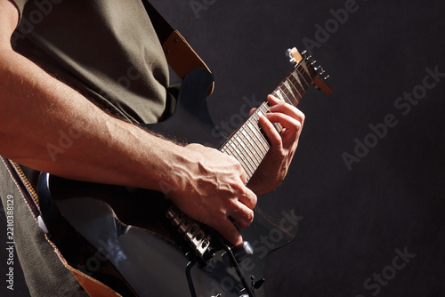 Posing hands of artist playing the black guitar on dark stage.