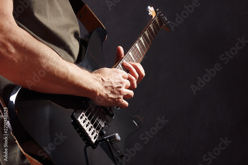 Hands of rock guitarist with black guitar on dark stage.