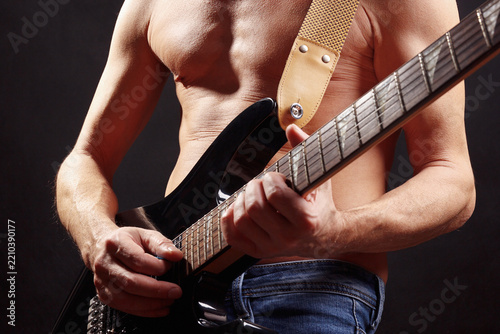 Musician playing solo on guitar on dark stage.