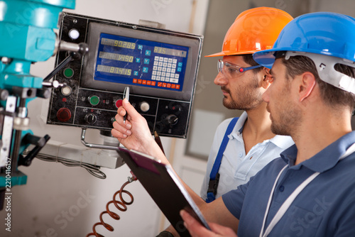 Close-up of industrial engineer pointing at control panel of milling machine with technician in manufacturing workshop.   