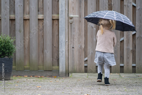 A young girl walks away holding an umbrella, seen from behind, symbolizing children's independence and self-reliance.