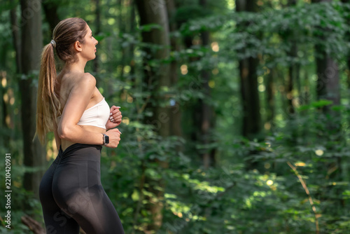 Woman running in woodland. Outdoor exercise with smartwatch and copy space.
