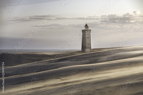 View of Rubjerg Knude lighthouse standing amidst shifting sand dunes under a soft sky in Lokken, Denmark.
