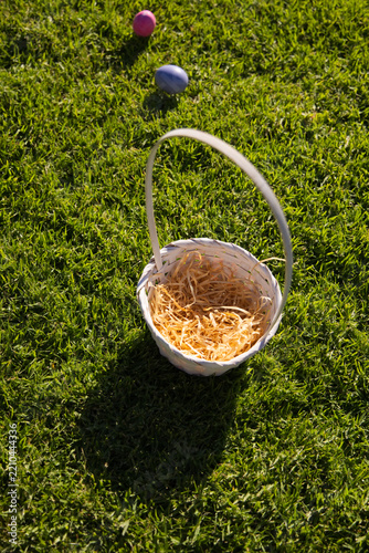 White wicker basket is sitting on green grass with shredded straw and pink and purple eggs