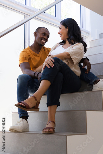 African American man and Asian woman sitting on tiled staircase facing partner near windows