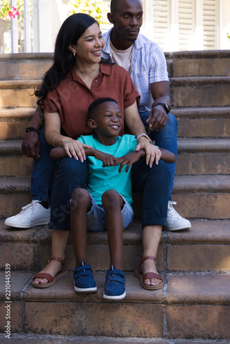 Diverse family sitting on stone steps at front entry, mother wearing rust blouse holding son