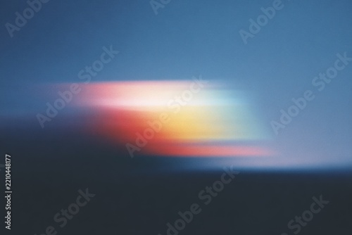 A blurry of a sunset over the ocean with the sky in a mix of blue red yellow and orange hues. the sun is setting in the background casting a warm orange glow across the sky.