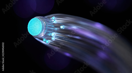 Macro photograph of small bundle of optical fiber with glowing blue light, purple reflection, and curved transparent strands against black background
