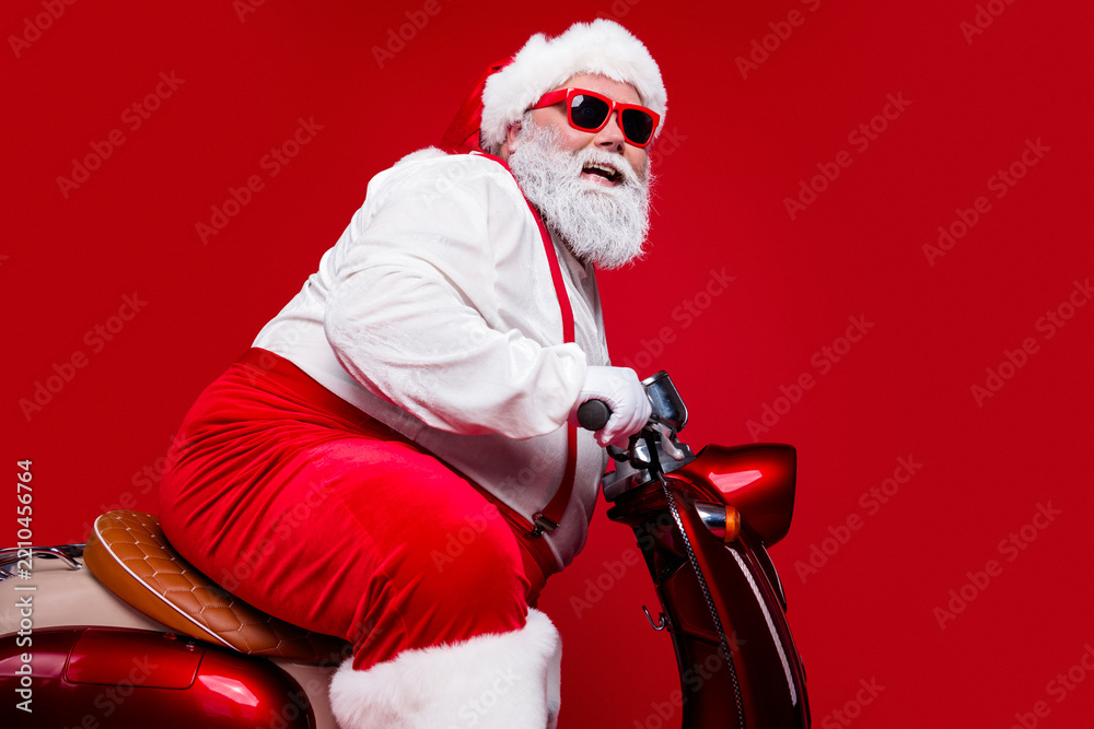 Obraz premium Santa Claus wearing sunglasses riding a red scooter for a fun and modern Christmas holiday portrait